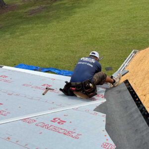 Coastline Roofing crew member installing roofing underlayment during a roof replacement project, with tools and safety gear on a residential rooftop.