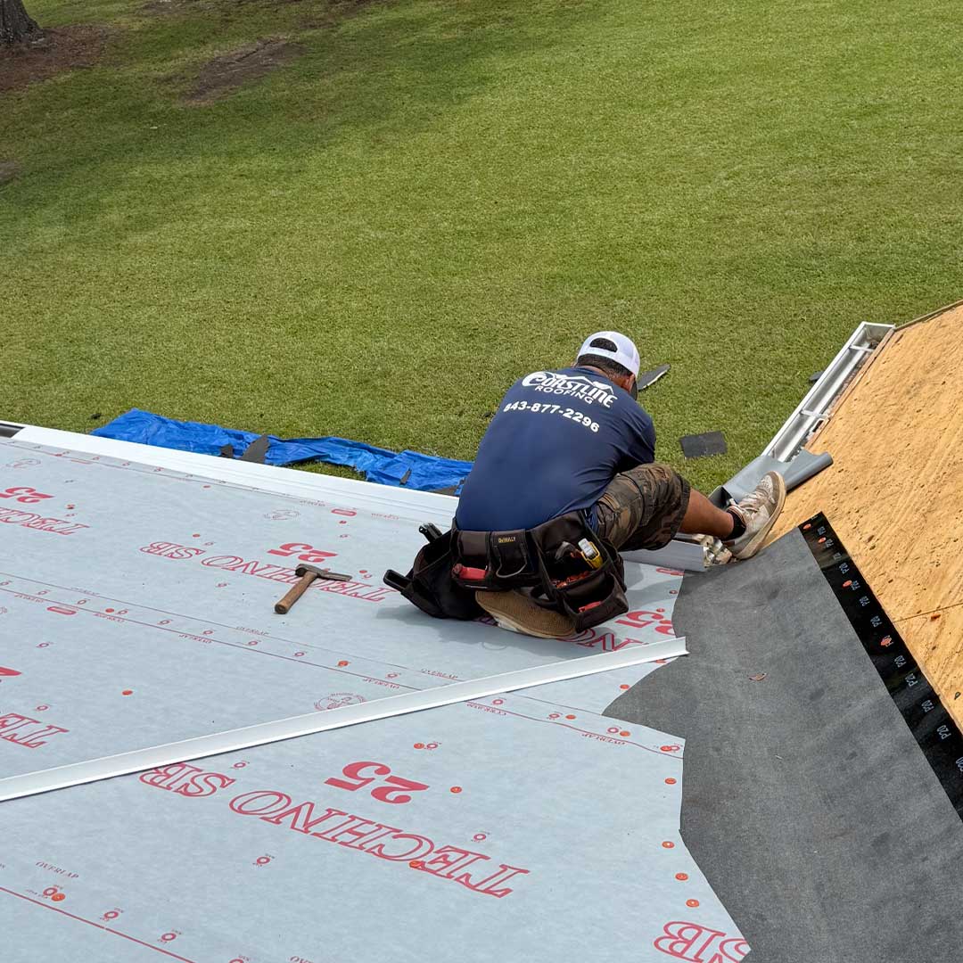 Coastline Roofing crew member installing roofing underlayment during a roof replacement project, with tools and safety gear on a residential rooftop.