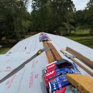 Roof installation in progress with synthetic underlayment being applied over exposed wooden decking, featuring GAF Timberline HD shingles and Pro-Start materials staged on the roof.