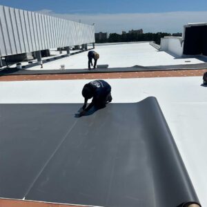 Crew members measure and cut TPO membrane on a commercial roof.