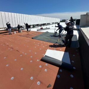 Roofer aligns TPO membrane along the roof surface during installation.