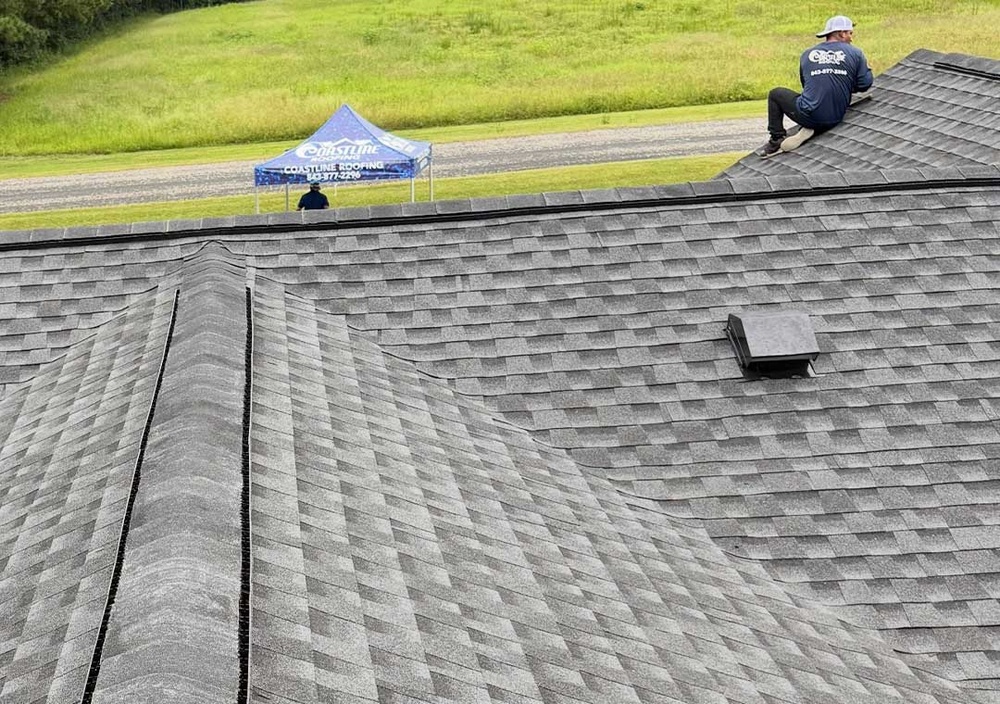 Roofer installing cap shingles and making final adjustments at roof edge during roof installation.